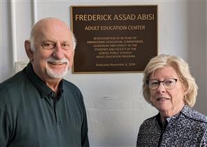 Fred Abisi and Betty McKiernan stand in front of the Frederick Abisi Adult Education Center dedication plaque